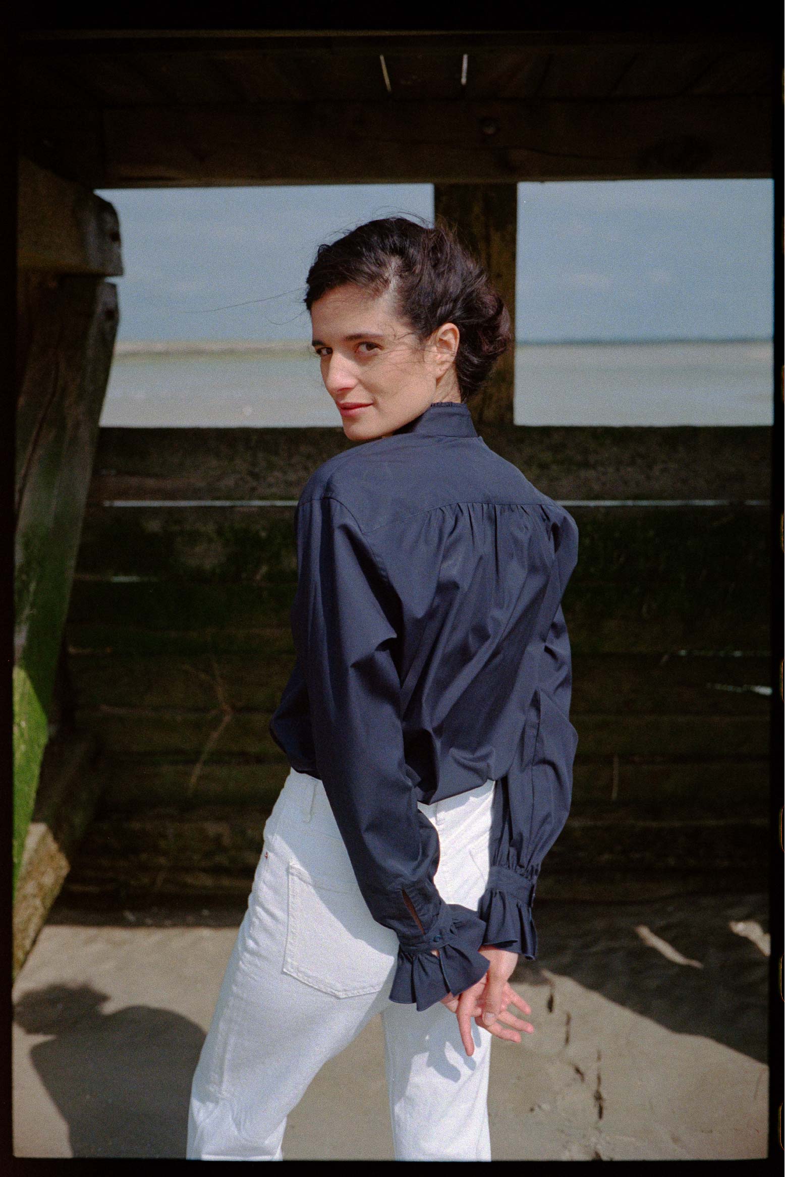 BOURRIENNE PARIS X: Photo vue de dos du mannequin, elle porte une chemise en popeline bleu marine et montre les détails des fronces qui se situent dans le dos de la chemise.