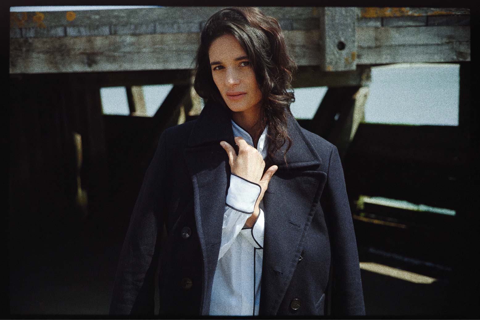 BOURRIENNE PARIS X: Mannequin portant un manteau long bleu marine, par-dessus une chemise en popeline blanche et avec un passepoil bleu marine le long de la gorge de boutonnage ainsi que sur les poignets. La photo met en avant le détail des poignets.