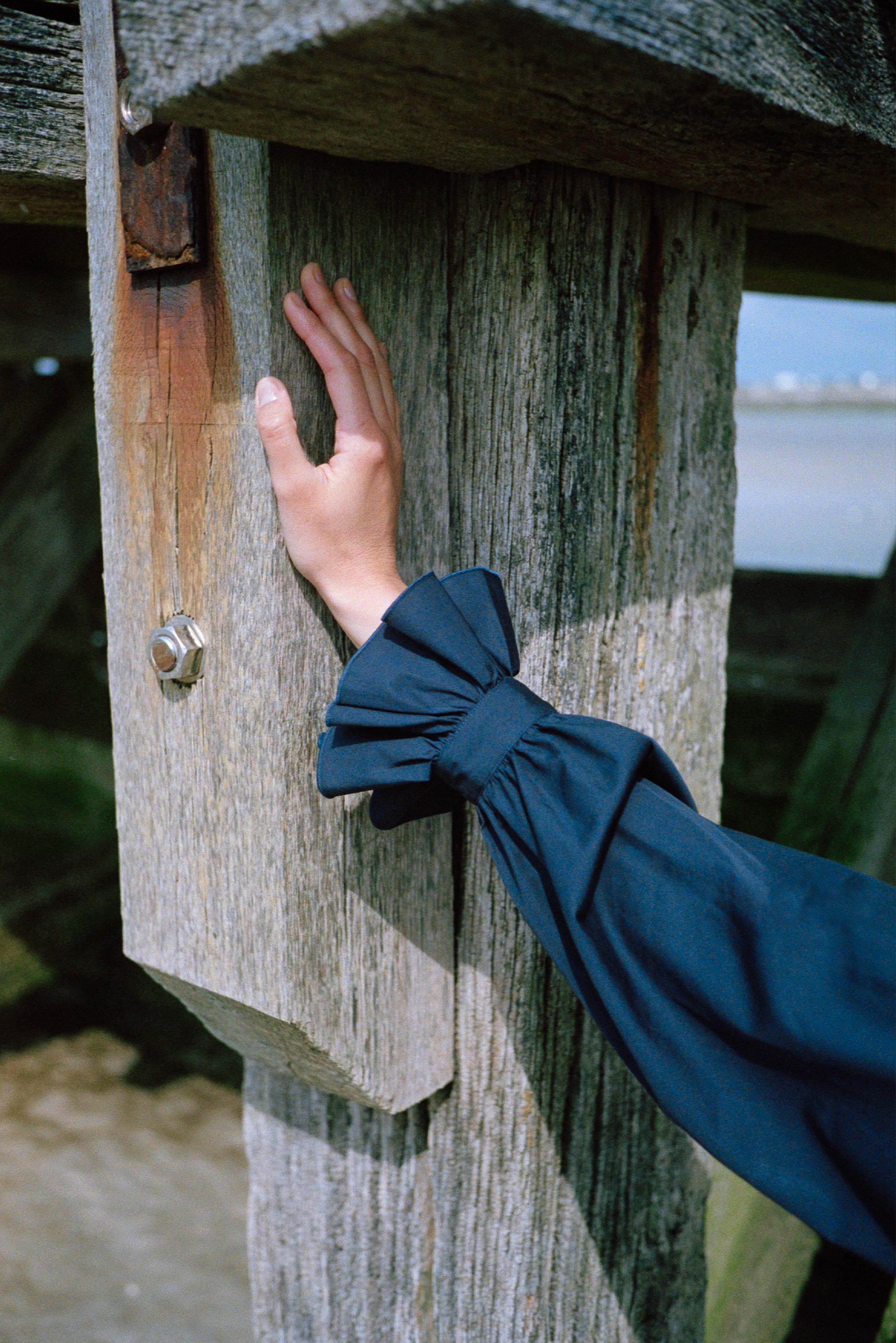 BOURRIENNE PARIS X: Photo close up du poignet, on voit seulement l’avant bras ainsi que la main du mannequin de manière à ce qu’on puisse apercevoir les détails des manches bouffantes et des volants brodés au niveau des poignets.