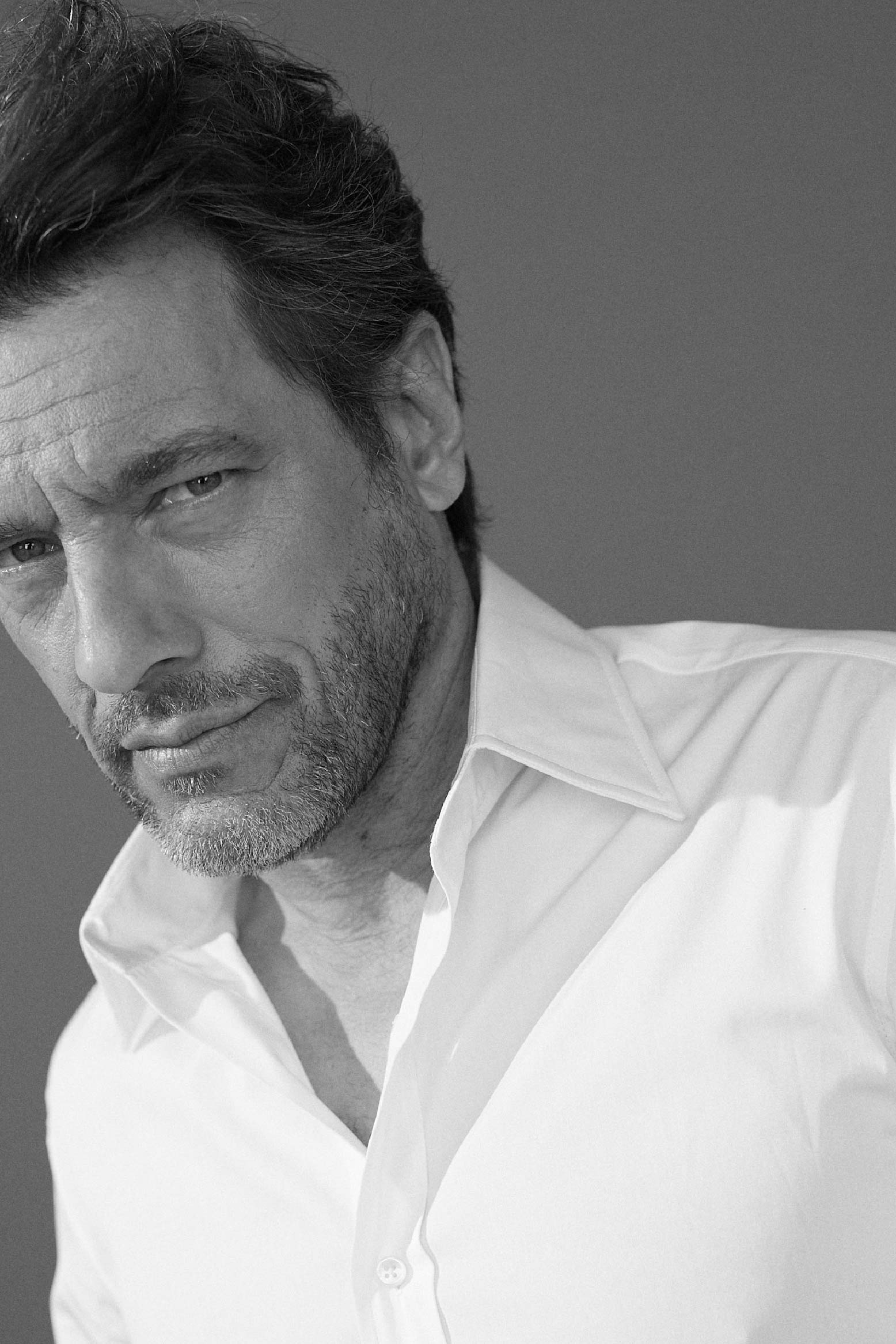 Photo noir et blanc plan serré d'un homme qui regarde l'objectif. Il porte une chemise blanche en popeline blanche double retors, poignets mousquetaires et col français.