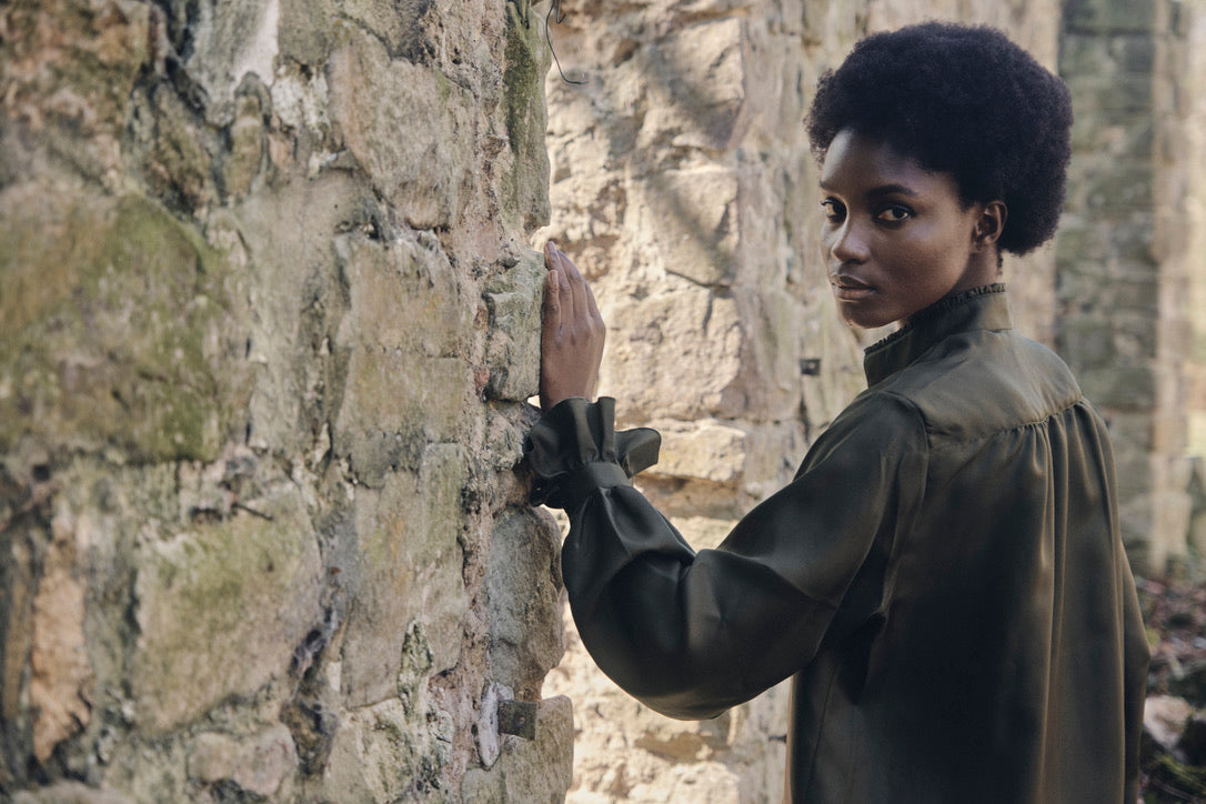 Chemise BOUDOIR Soie Kaki portée par une mannequin posant devant un mur en pierres.