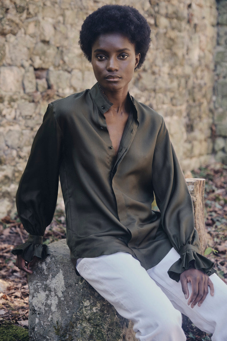 Femme assise portant la chemise BOUDOIR en soie couleur kaki, légèrement déboutonnée.