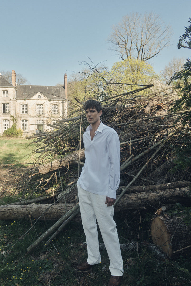 Photo plein pied d'un homme portant une chemise qui se nomme VOYAGE, elle est en 100% Coton, fabriqué en Europe, une coupe Bourrienne, un col Français et des poignets Bourrienne. Il porte également un pantalon en lin blanc et des mocassins marrons.