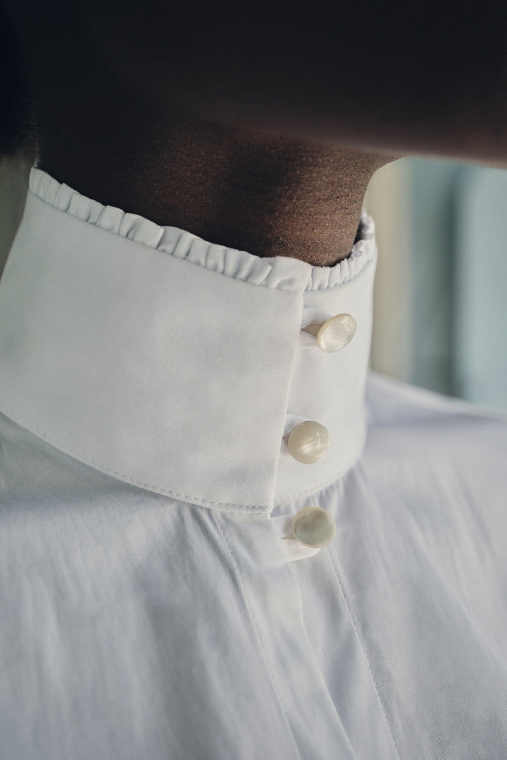 Close-up sur le cou de la mannequin portant la chemise PRÉCIEUSE, col fermé par trois boutons ronds en nacre.