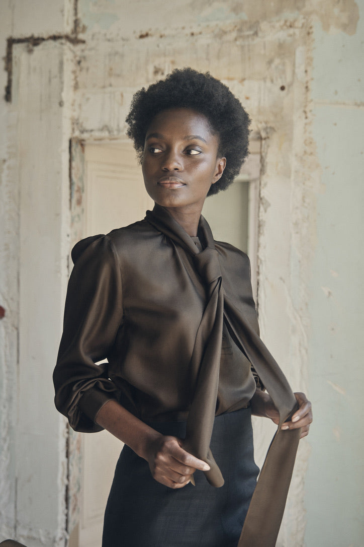 femme portant la chemise COMTESSE en soie couleur kaki, elle tient le col écharpe noué en cravate dans ses mains.