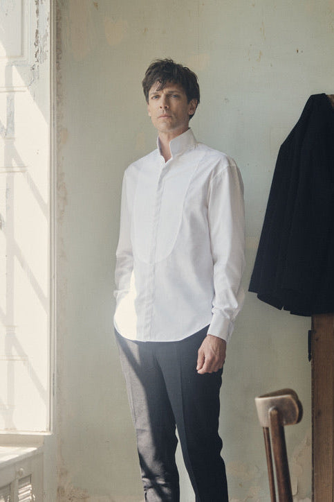 Photo plan américain d'un homme debout portant une chemise blanche, avec des poignets Français, une chemise à la coupe Bourrienne, un col haut officier avec un plastron.