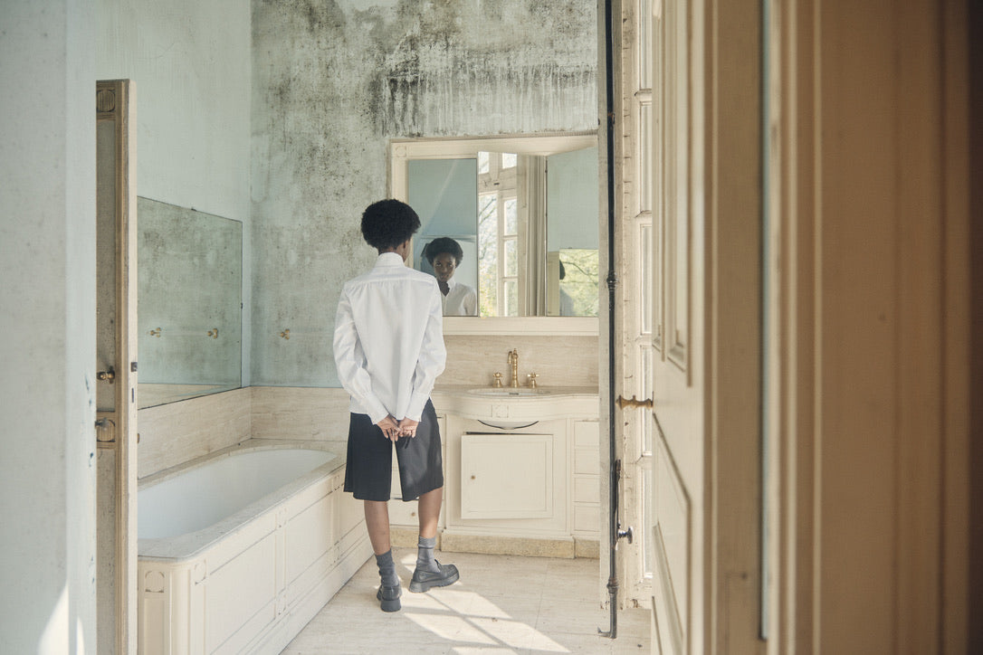 Femme de dos dans une salle de bain, vêtue d'une chemise blanche Bourrienne Paris X.