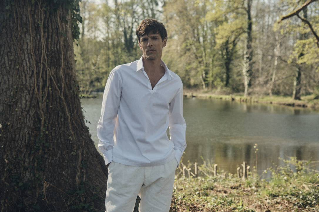 Photo plan taille d'un homme portant une chemise qui se nomme VOYAGE, elle est en 100% Coton, fabriqué en Europe, une coupe Bourrienne, un col Français et des poignets Bourrienne. Ses deux mains sont rentrées dans ses poches de pantalons.