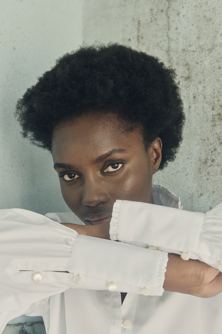 Close-up sur les poignets longs de la chemise PRÉCIEUSE, devant le visage de la mannequin.