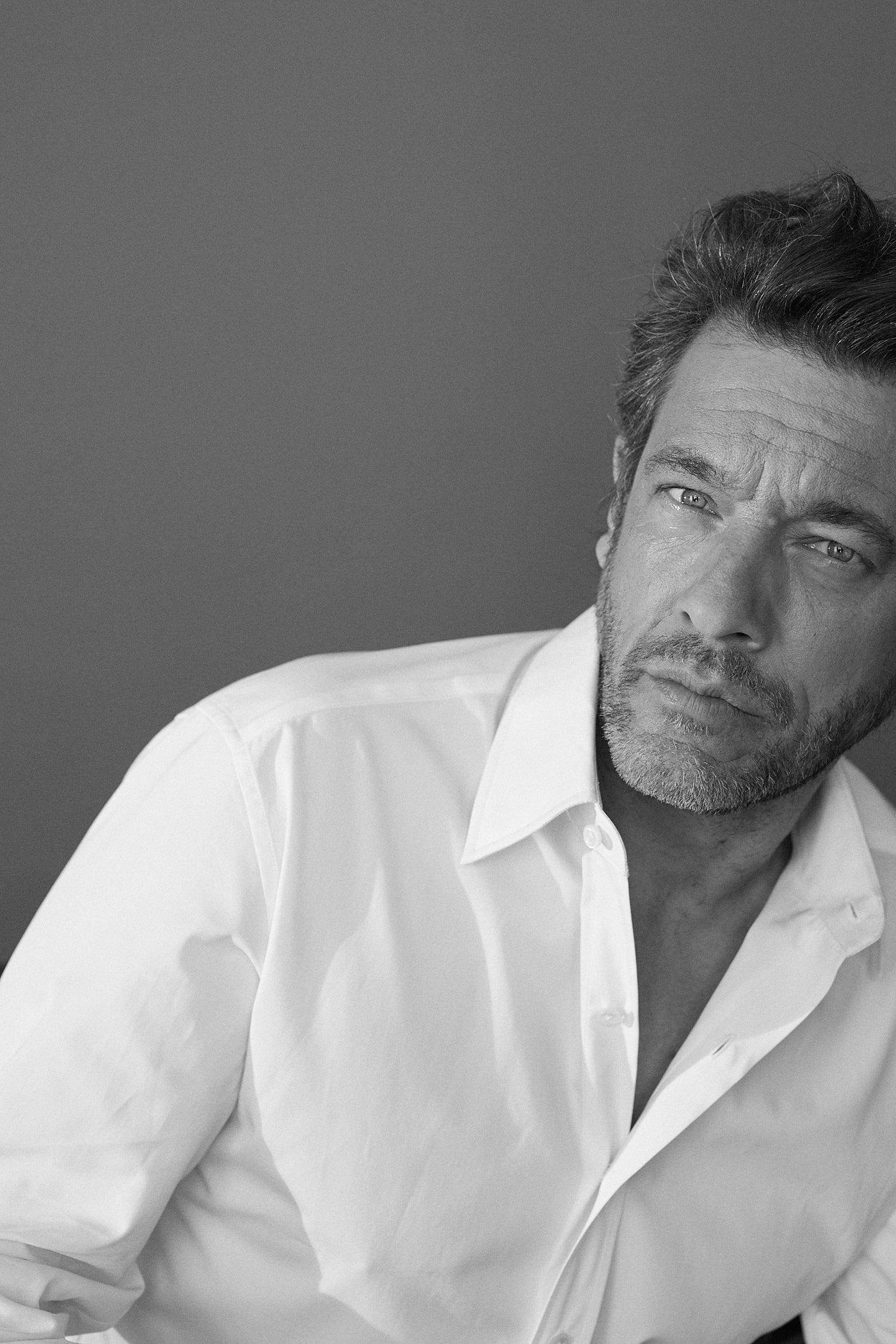 Photo noir et blanc plan serré d'un homme qui regarde l'objectif. Il porte une chemise blanche en popeline blanche double retors, poignets mousquetaires et col français.