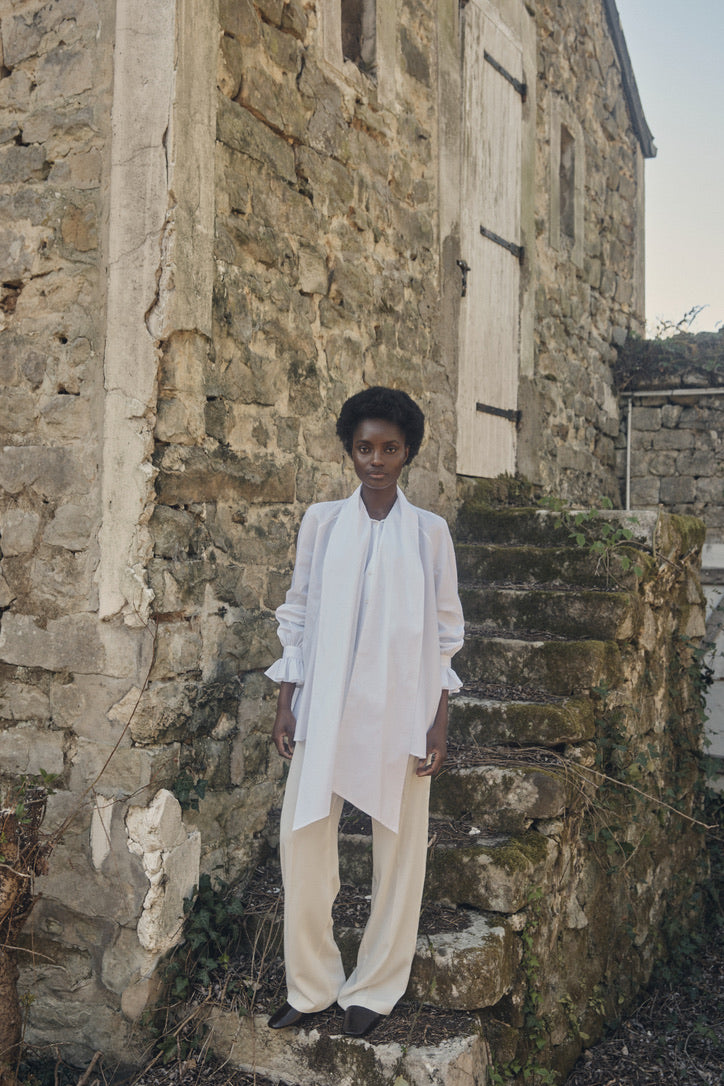 Mannequin portant la chemise Céleste sur des escaliers en pierre en extérieur, col lavallière détaché, plan plein pied.
