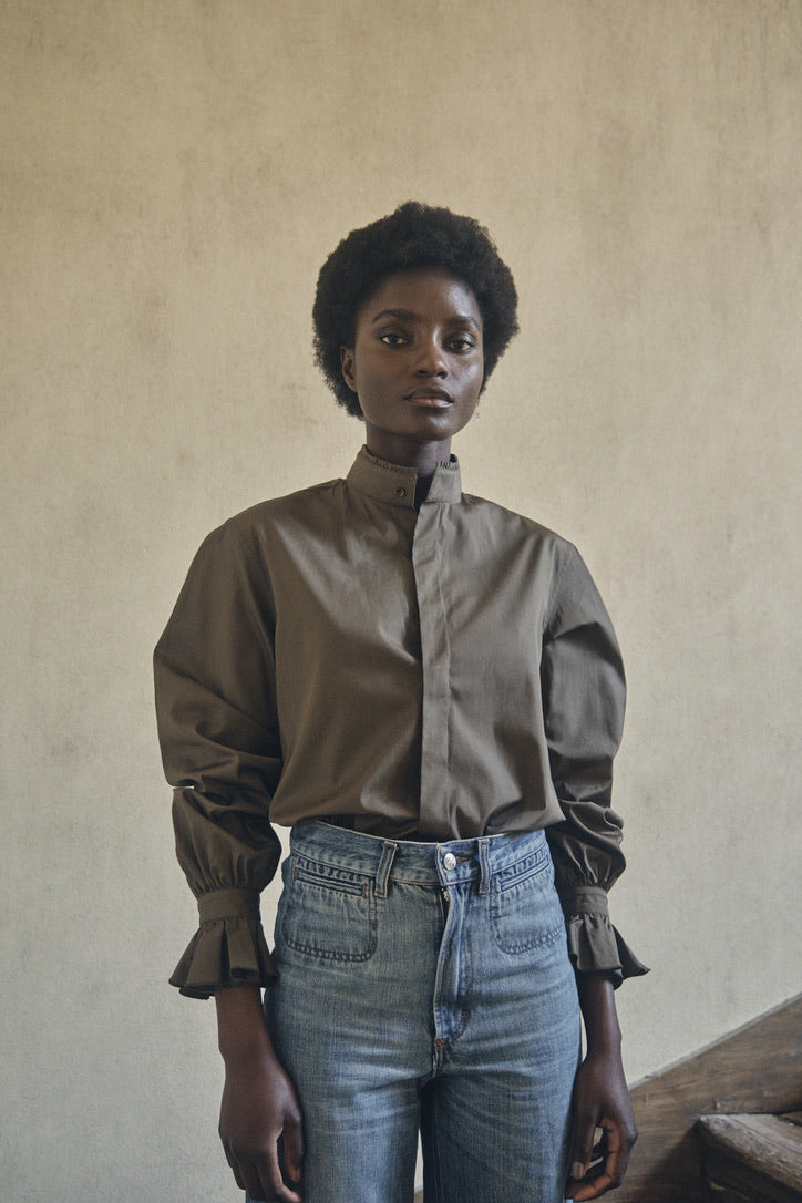 Chemise BOUDOIR Kaki rentrée dans un jean bleu, portée par une mannequin dans les escaliers d'une maison.
