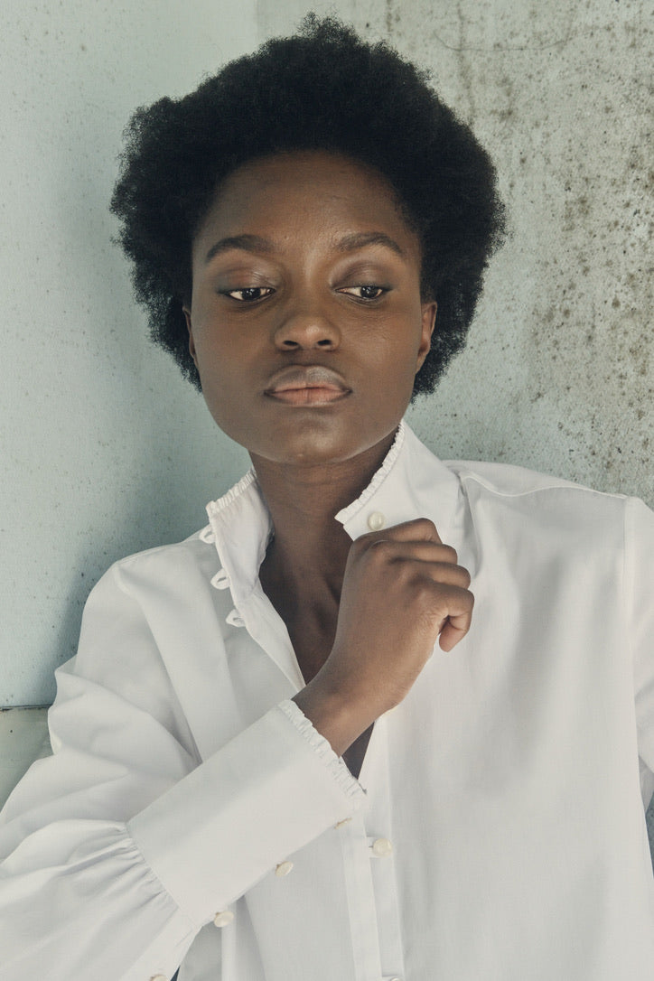Femme tenant dans sa main le col de la chemise blanche PRÉCIEUSE.