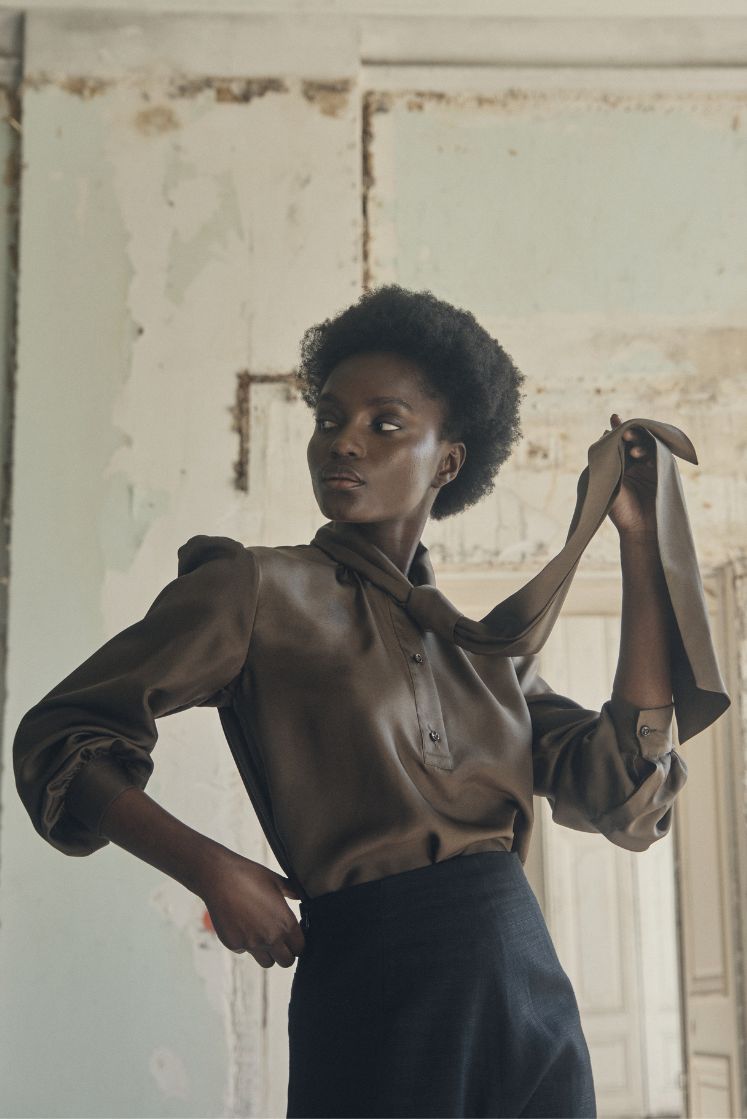 mannequin portant une chemise en soie couleur kaki, tenant dans la main son col lavallière noué en cravate