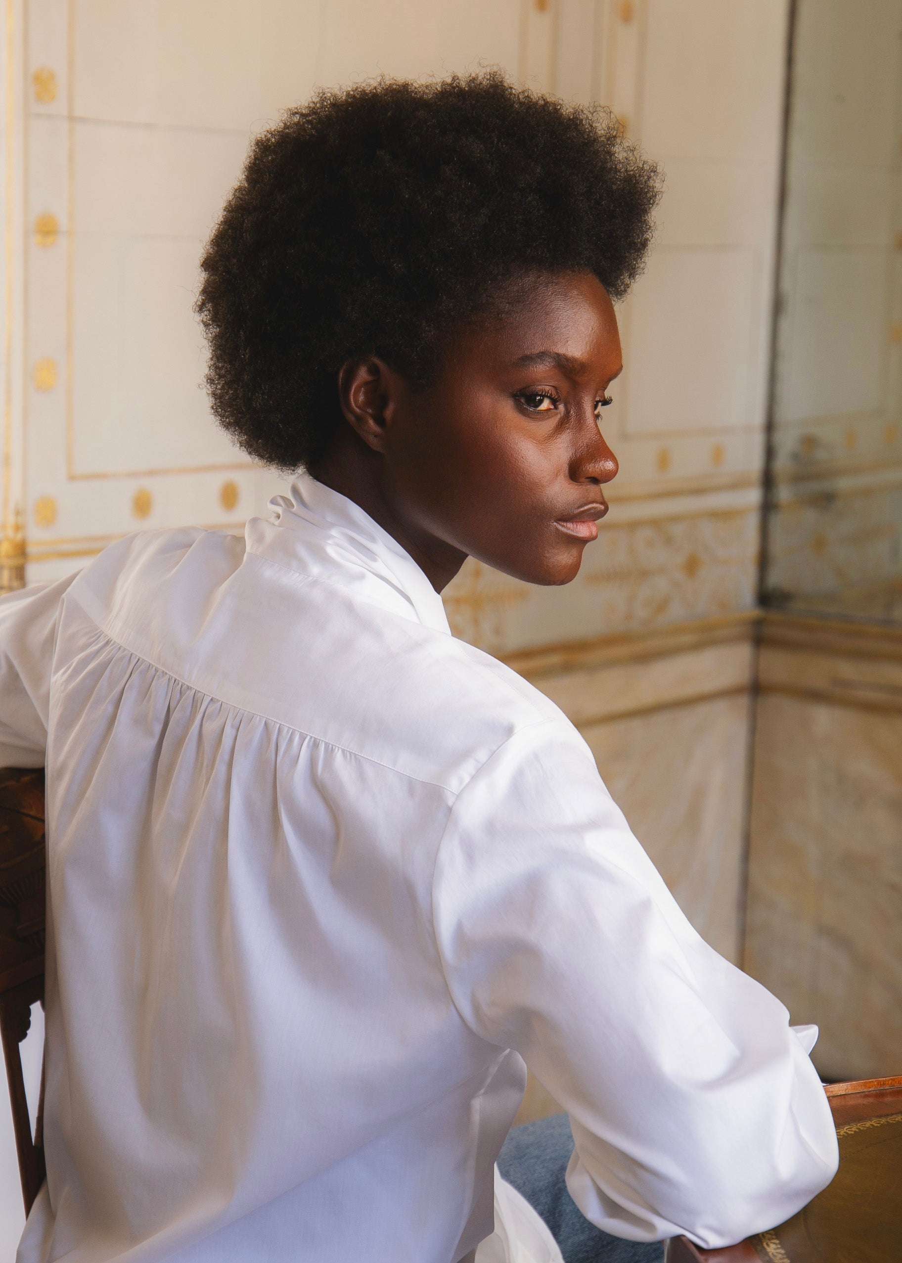 Mannequin de dos assise sur une chaise posant dans l'Hôtel de Bourrienne avec la chemise EXQUISE, dos de la chemise avec de délicates fronces.