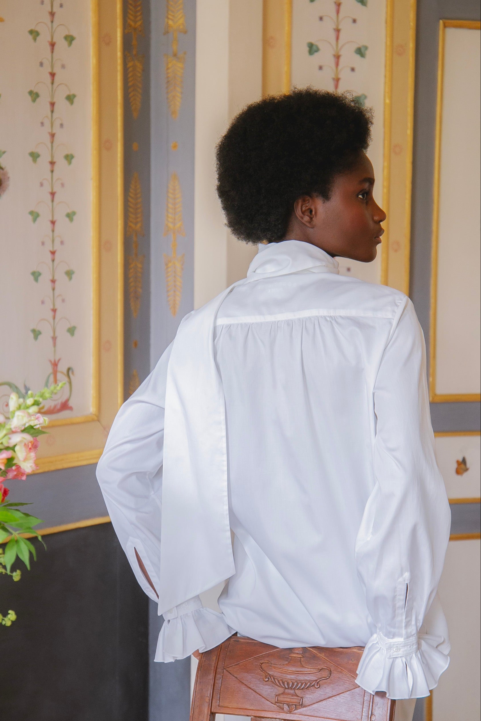 Mannequin de dos appuyée sur une chaise posant dans l'Hôtel de Bourrienne avec la chemise EXQUISE, poignets à volants.