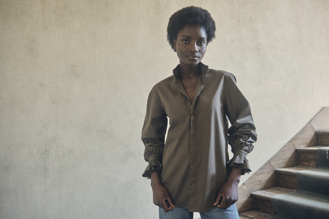 Plan américain d'une femme portant la chemise BOUDOIR couleur Kaki posant dans les escaliers d'une maison.