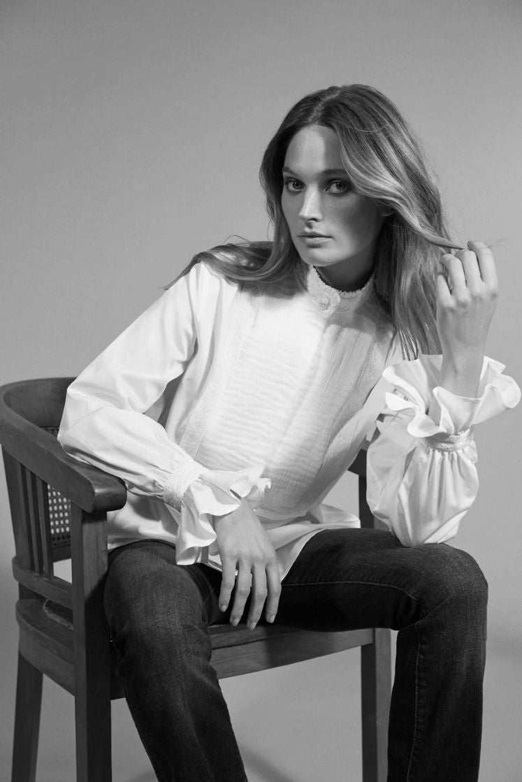 Femme assise sur une chaise portant la chemise DIVINE, photo en noir et blanc.