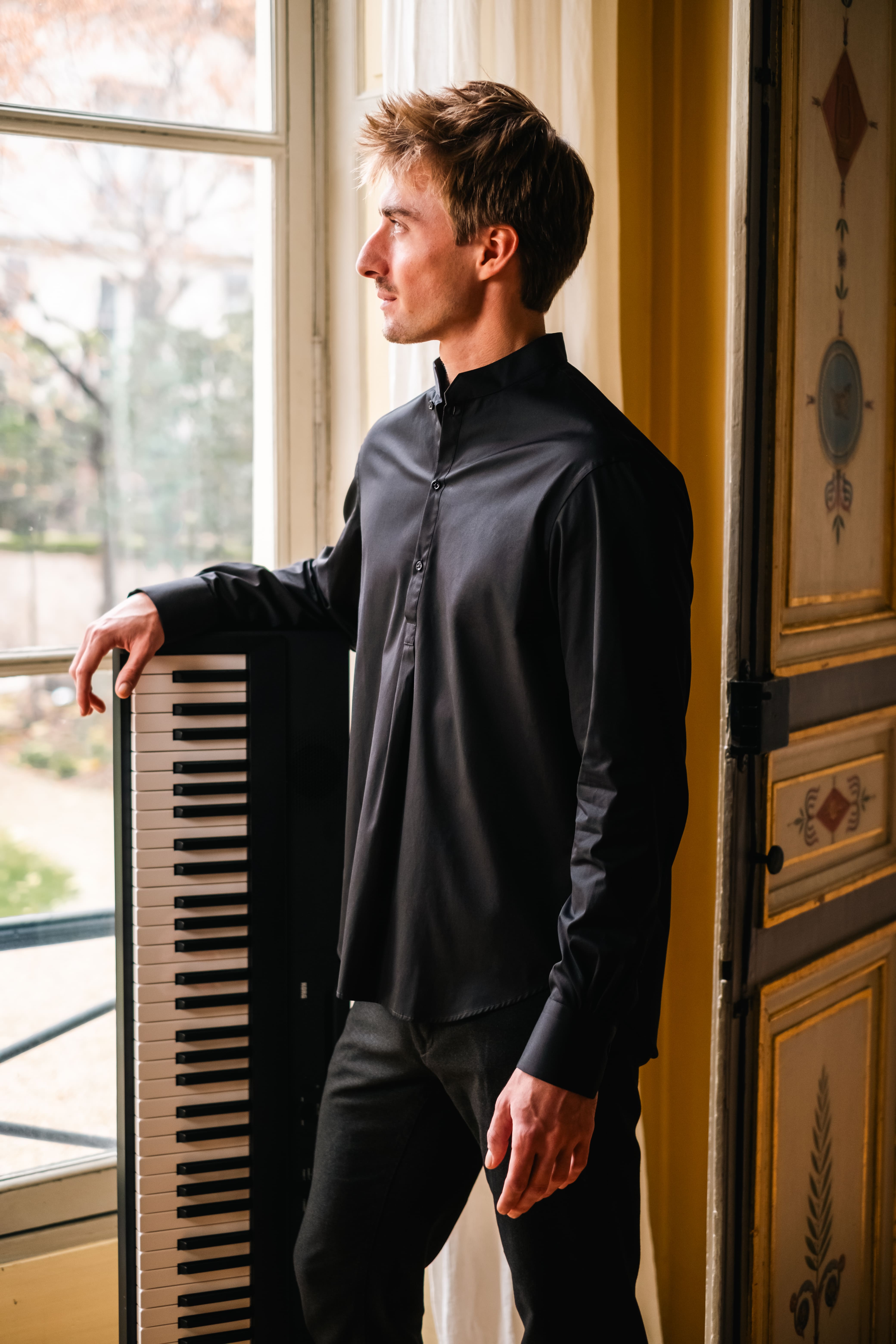 La chemise ÉPICURIEN noire portée par un pianiste dans l'Hôtel de Bourrienne : coupe Bourrienne, col officier, poignets classiques.