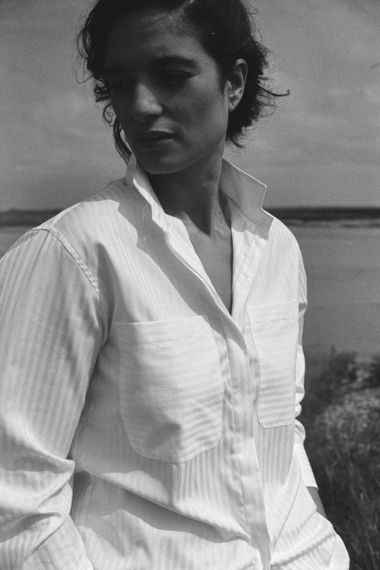 Photo vue de face et de près du mannequin, elle porte une chemise en coton et à rayures blanches ton sur ton. On aperçoit les détails du col haut et des poches plaquées.