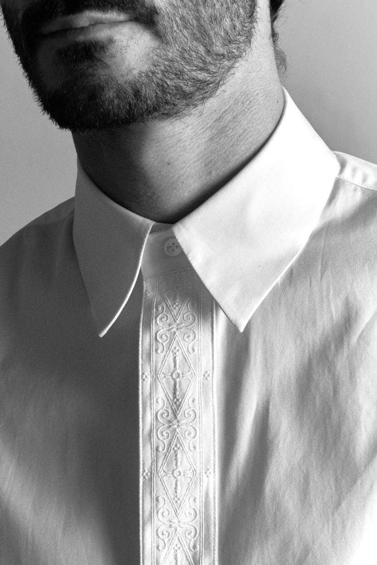 Homme portant une chemise blanche à col français signée d'une gorge de boutonnage avec un galon brodé.