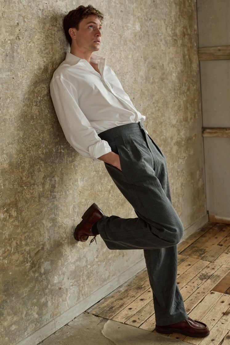 Homme portant le pantalon HORIZON gris, adossé contre un mur.