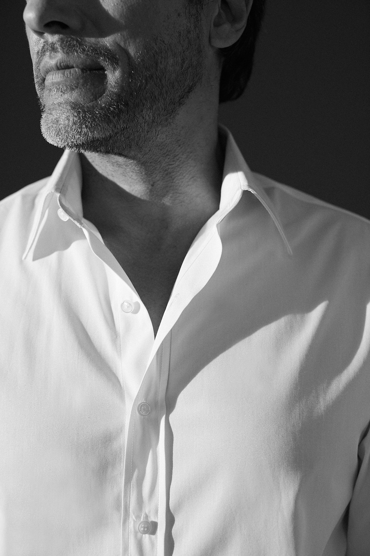 Photo noir et blanc plan serré d'un homme, il porte une chemise blanche en popeline blanche double retors, poignets mousquetaires et col français. On aperçoit que le bas de son visage, jusqu'à son nez.