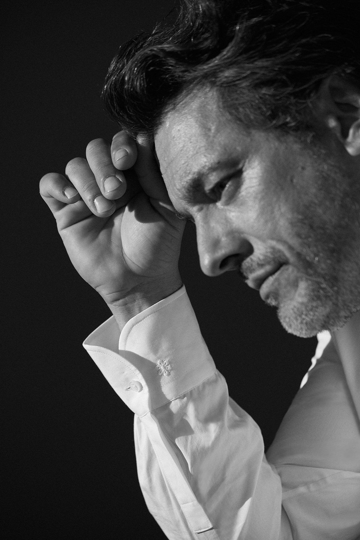 Photo noir et blanc gros plan, d'un homme de profil sa main droite touche son front. Il porte une chemise blanche en popeline double retors avec des poignets classiques. On voit en deuxième plan son poignet où l'on voit le logo brodé de la fleur Bourrienne.