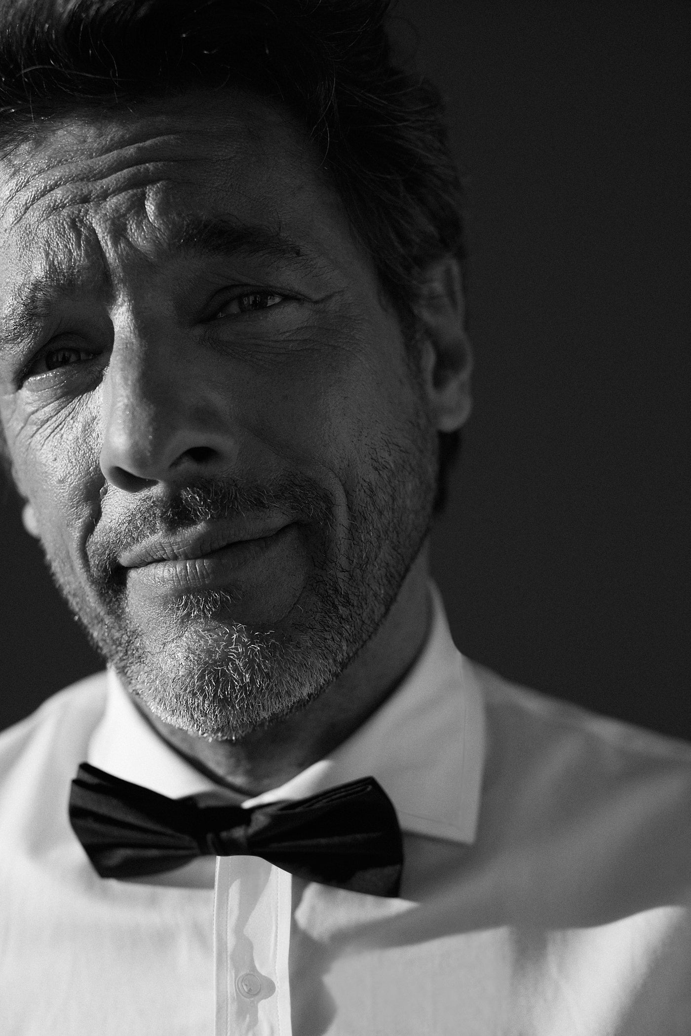 Photo gros plan d'un homme qui sourit légèrement sans laisser apparaître ses dents. Il porte une chemise col italien, on aperçoit en premier plan le col italien et un noeud papillon noir attaché au col italien.