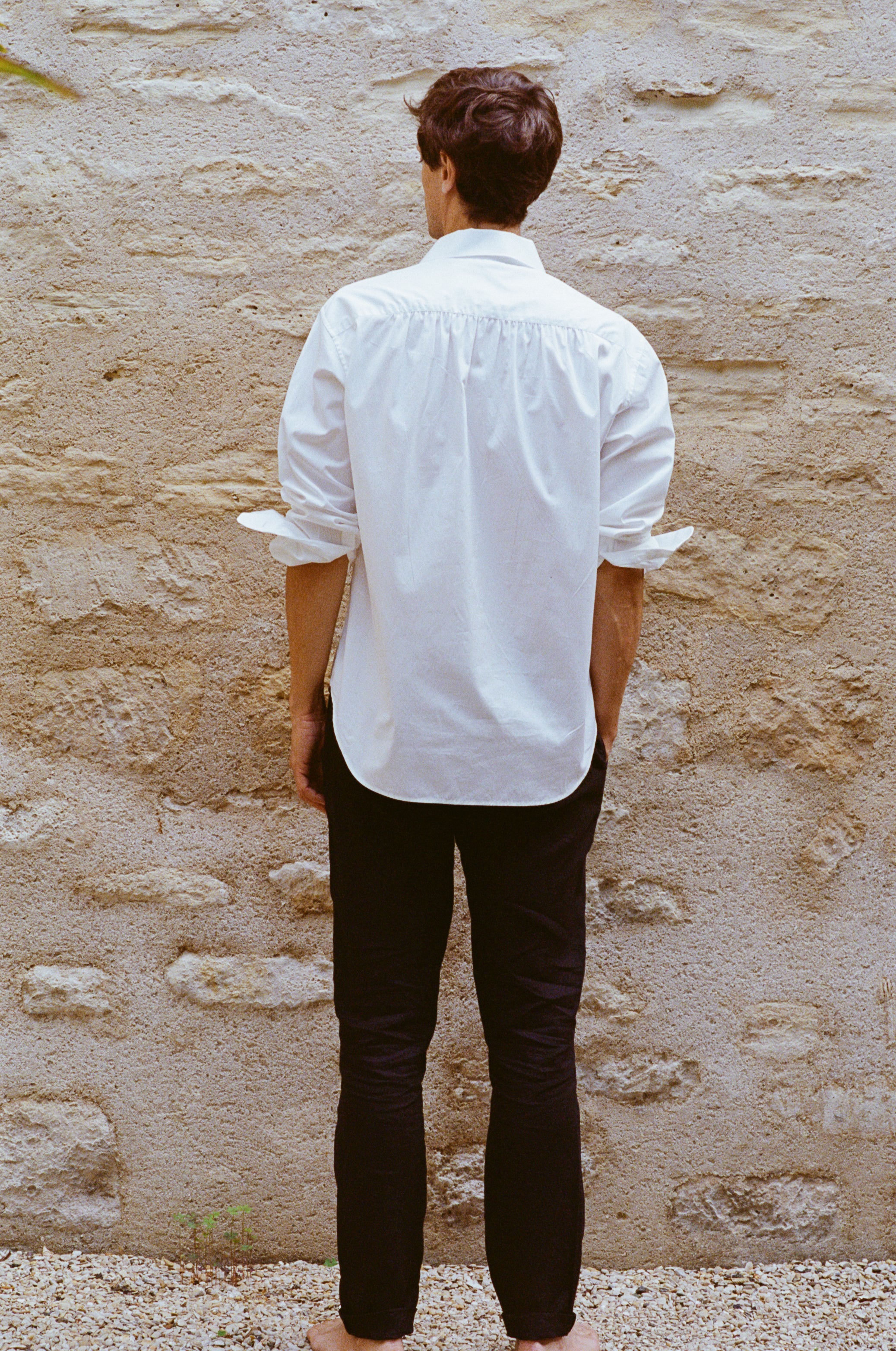 Homme portant une chemise blanche élégante aux manches retroussées, de dos, avec des fronces dans le dos.