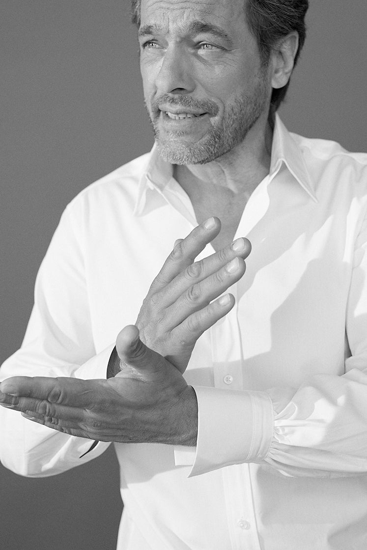 Photo noir et blanc plan poitrine d'un homme portant une chemise en popeline blanche double retors, col français et poignets bourrienne. L'homme est debout il croise ses mains, la voit bien les details de sont poignet gauche avec les fronces qui debute sur la chemise du poignet.