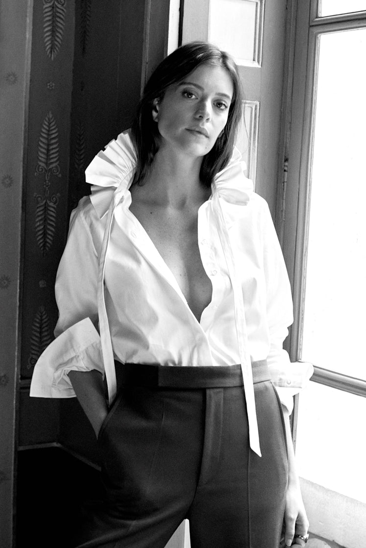 Femme adossée contre un mur dans l'Hôtel de Bourrienne, portant la chemise PASTEL blanche en popeline de coton, avec un grand col à volants.