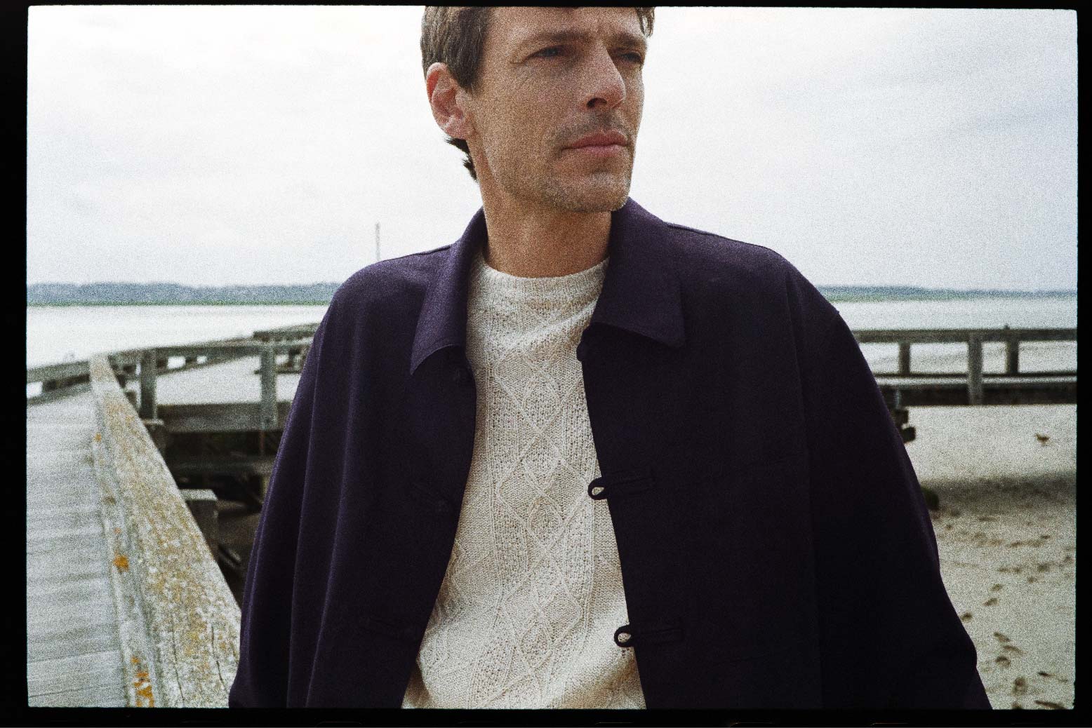 BOURRIENNE PARIS X: Photo prise de face, close up sur le devant de la veste, le mannequin regarde à l’horizon et porte une veste bleu marine à col français et au boutonnage travaillé, disposant de trois poches plaquées à l'avant.