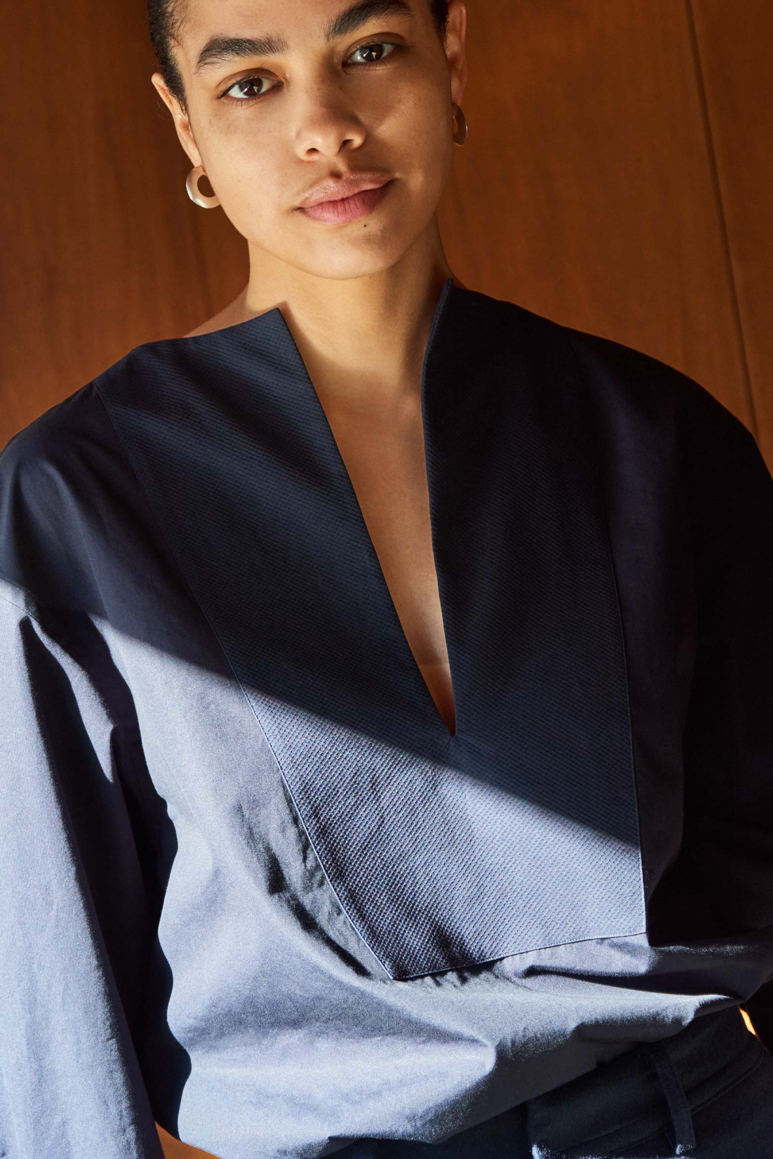 Photo prise de face, le mannequin regarde la caméra, porte une chemise en popeline bleu marine et on s’aperçoit parfaitement du plastron en ogive qui allonge la silhouette.