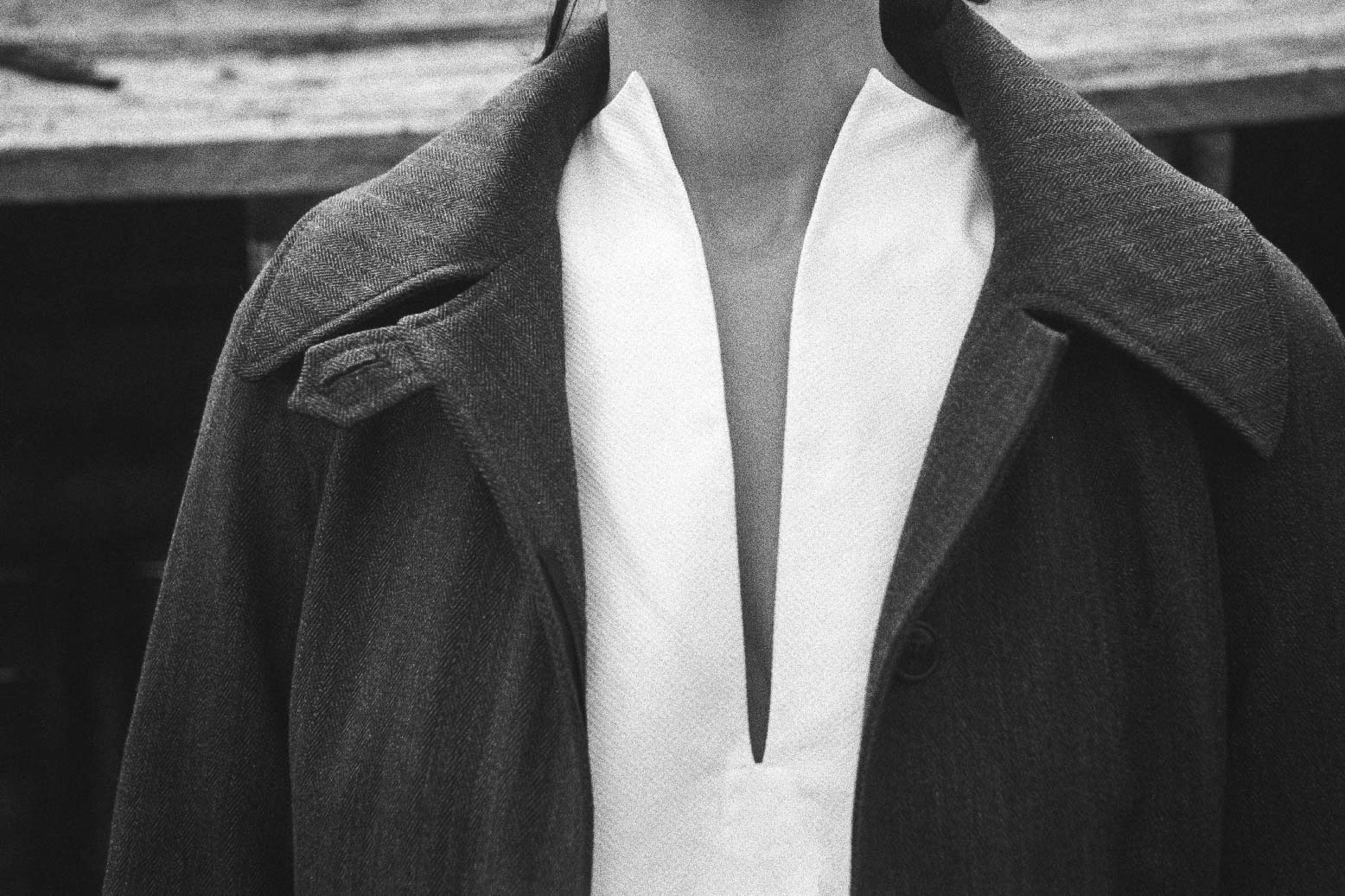 BOURRIENNE PARIS X: Photo close up du devant de la chemise: chemisier est non boutonné et a un décolleté fendu est orné de part et d'autre d'un plastron en ogive qui allonge la silhouette. Le mannequin porte un manteau foncé.