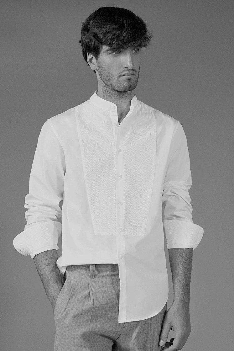 Homme posant en chemise blanche à plastron Bourrienne Paris X, avec un col officier et ses manches retroussées.