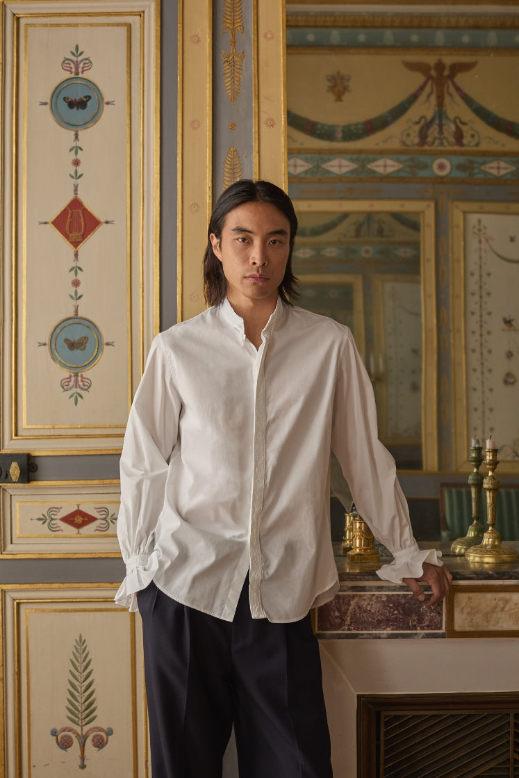 Homme portant la chemise BOUDOIR, dans l'Hôtel de Bourrienne : galon brodé sur la ligne de boutonnage, poignets à volants, col ancien bordé de petits volants.