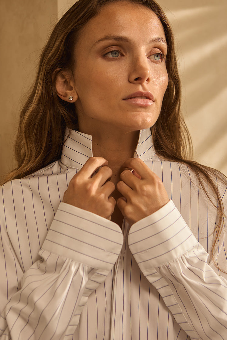 Closeup d'une femme tenant le col de la chemise AMAZONE à rayures bleu marine.