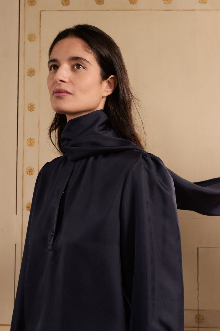 Femme brune portant la chemise COMTESSE en soie bleu marine avec le col lavallière enroulé autour du cou.