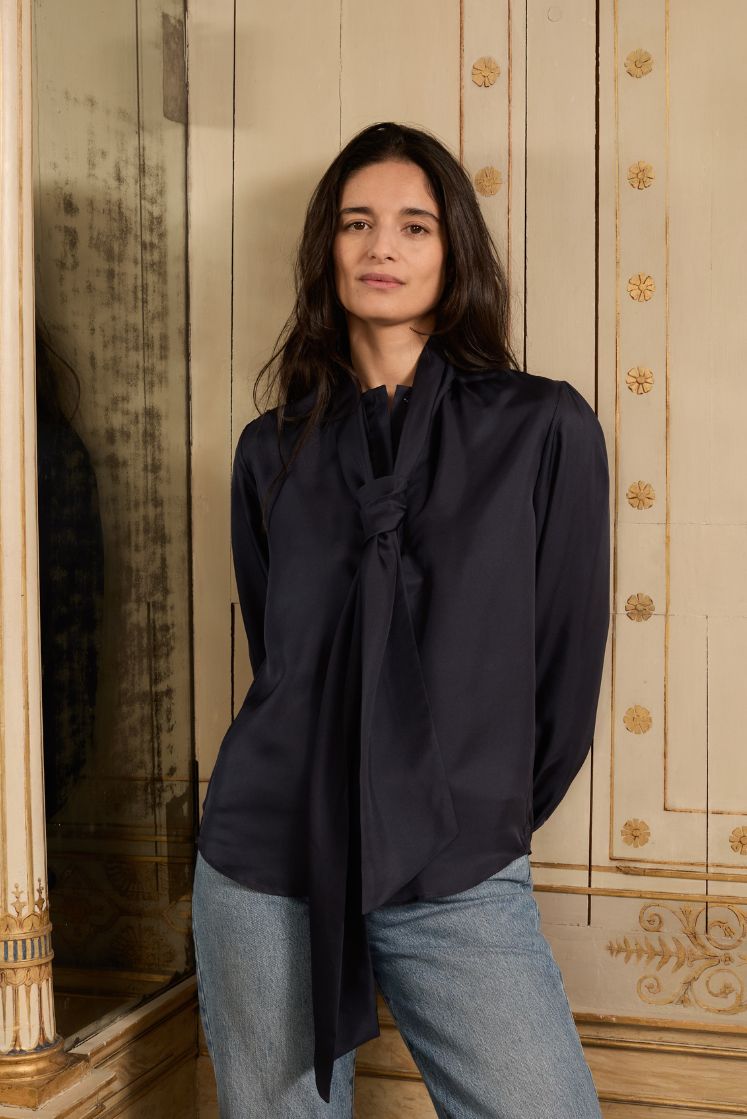 Femme brune portant la chemise COMTESSE en soie bleu marine avec le col lavallière noué en cravate.