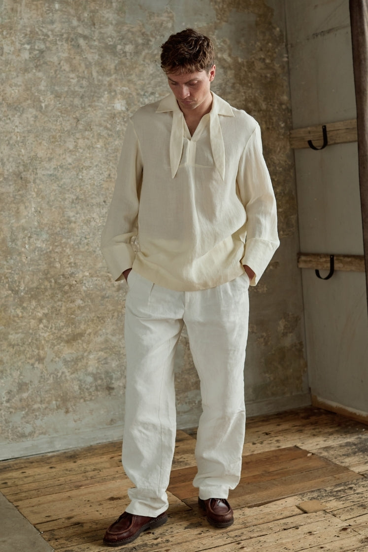 Homme portant la chemise blanche DOCK en lin et laine, col français à foulard intégré inspiré des vareuses, les mains dans les poches, plan plein pied de face.
