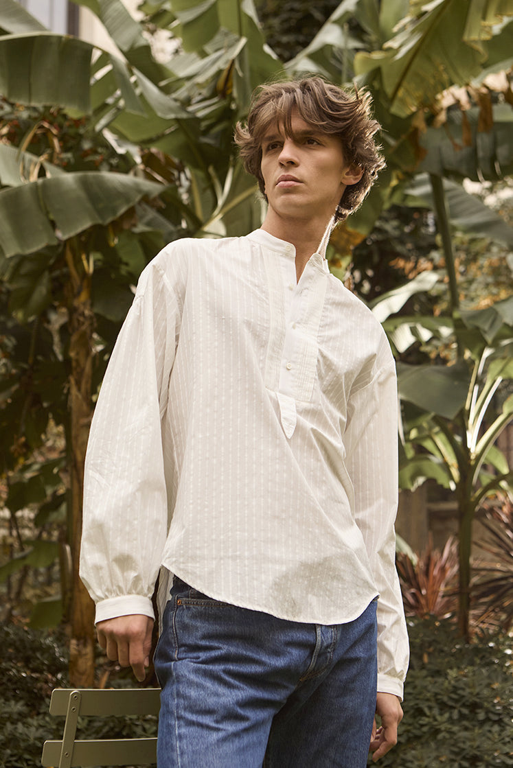 chemise blanche ample pour homme à col officier avec rayures blanches portée par un mannequin dans un jardin