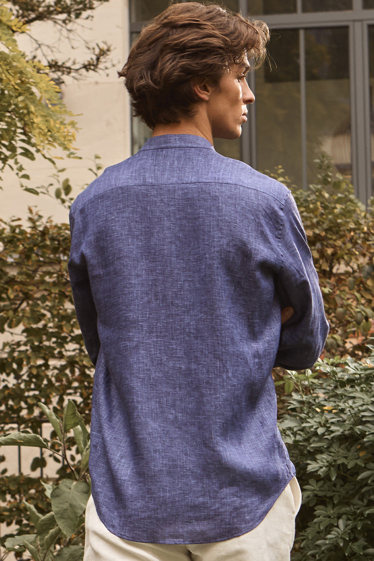 Homme dans un jardin portant la chemise NOCTURNE en lin bleu de dos.