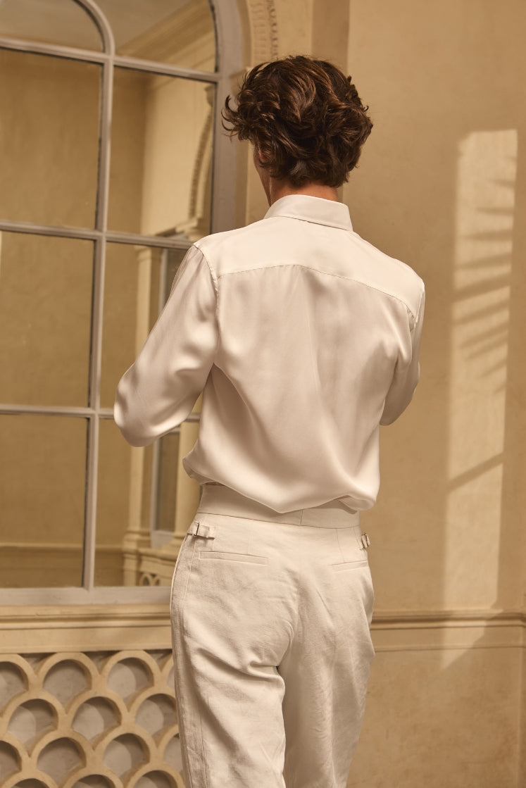 Homme de dos portant une chemise en soie blanche rentrée dans un pantalon en lin blanc.