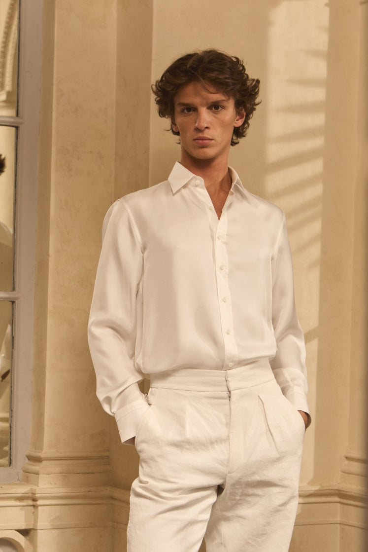 Homme portant une chemise en soie blanche avec un col français, rentrée dans un pantalon en lin blanc.