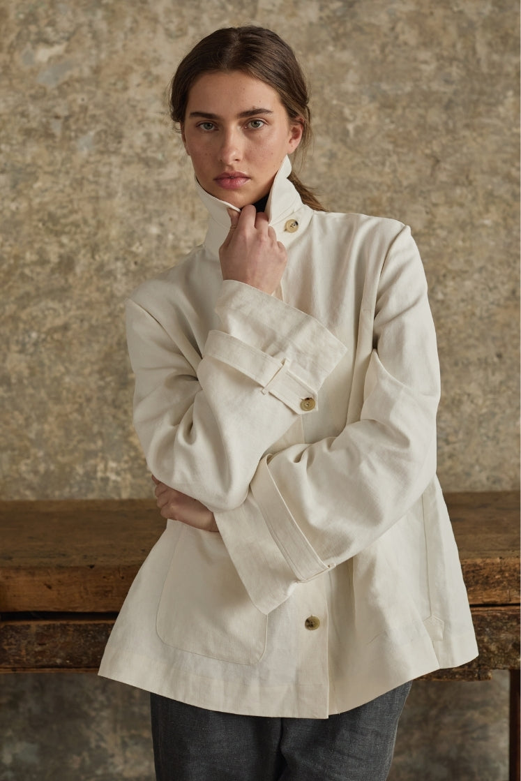 Femme portant la veste blanche PIGMENT, tenant le col haut, lin plâtré signature