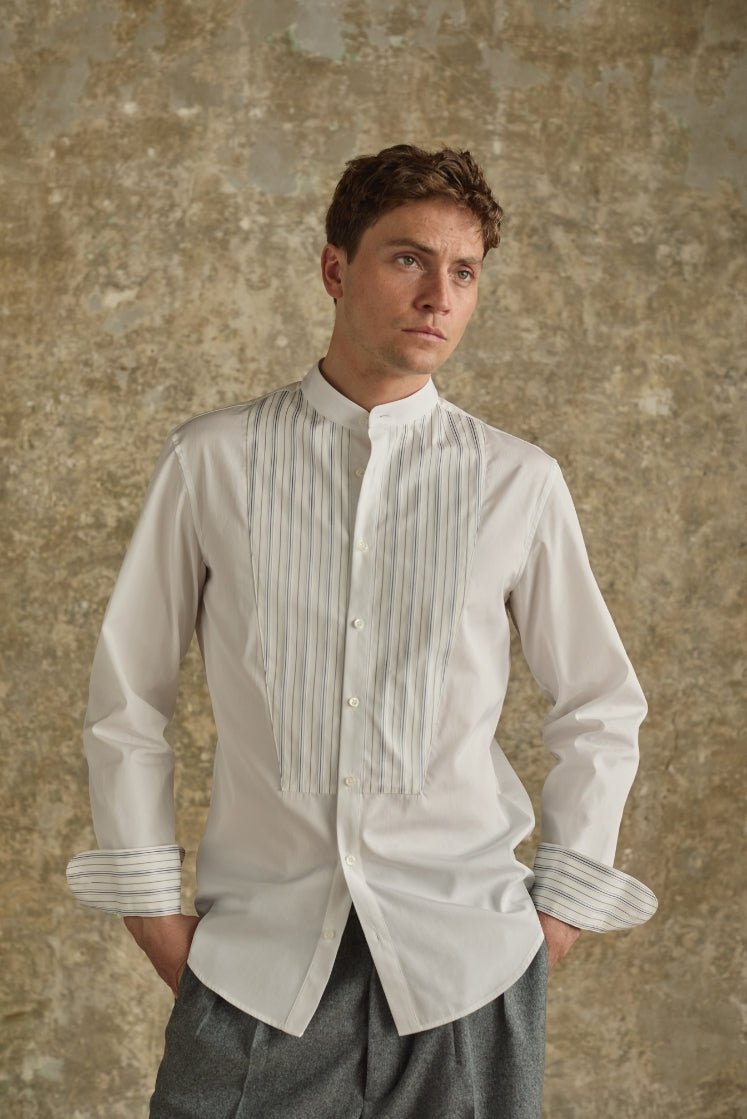 Homme portant la chemise ROMANCIER blanche en popeline de coton italienne double retors avec un col officier, un plastron rayé et des revers de poignets rayés bleu et gris.