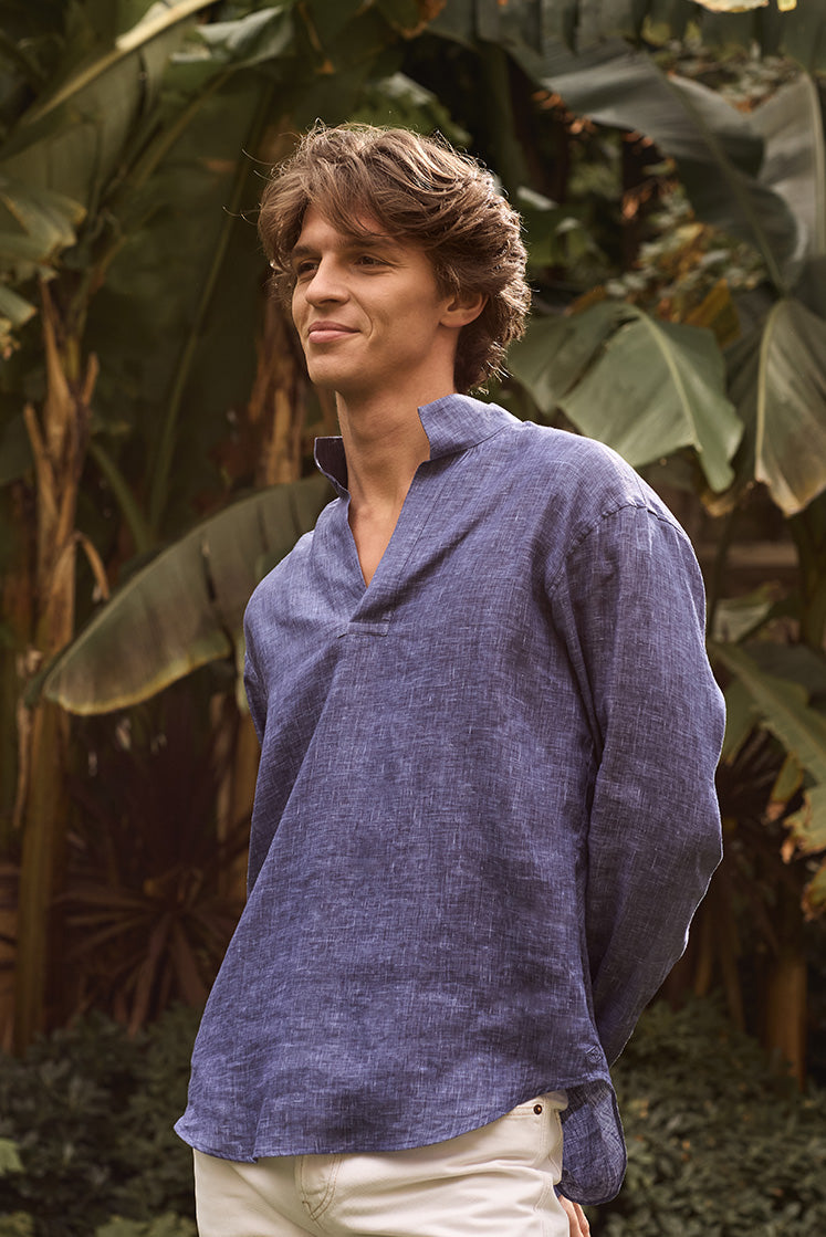 Homme souriant dans un jardin portant une chemise en lin bleu marine à col haut.