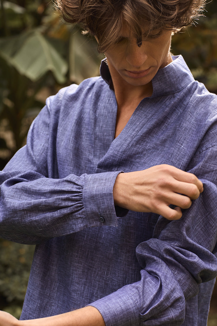 Homme remontant la manche de sa chemise en lin bleu navy à col haut et poignets classiques.