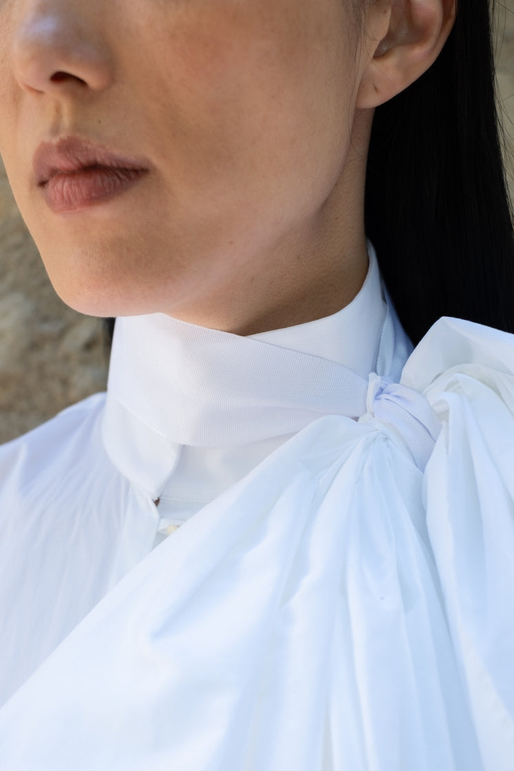 Closeup sur le col haut de la chemise Juliette, avec la fleur sculptée en tissu nouée autour du cou.